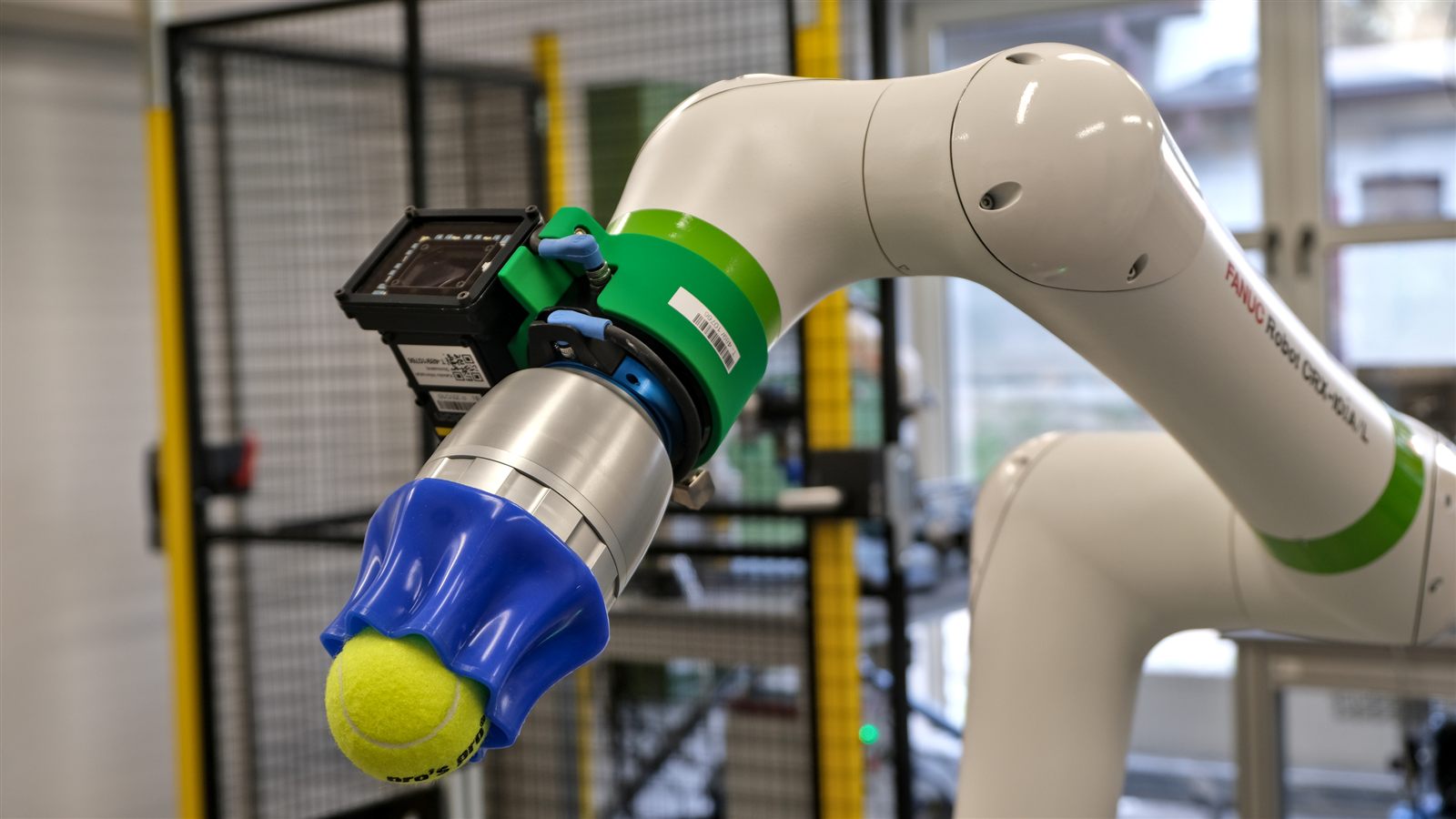 Cobot FANUC CRX z kamerą i niebieskim chwytakiem trzymającym piłkę tenisową.