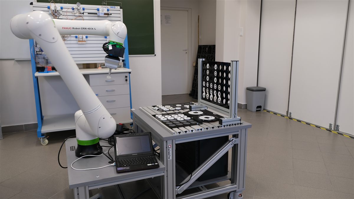 Stanowisko z cobotem FANUC CRX, panelem operatorskim i tablicą elementów do manipulacji.